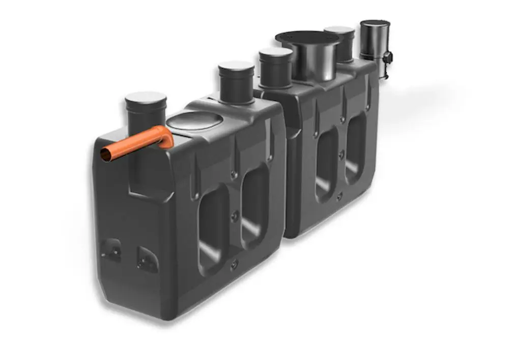 Roth Produkt mit zwei Behältern, einem orangefarbigen Rohr, mehreren Öffnungen und einem Deckel. Dient wahrscheinlich zur Installation oder Nachrüstung in einem Haussystem.